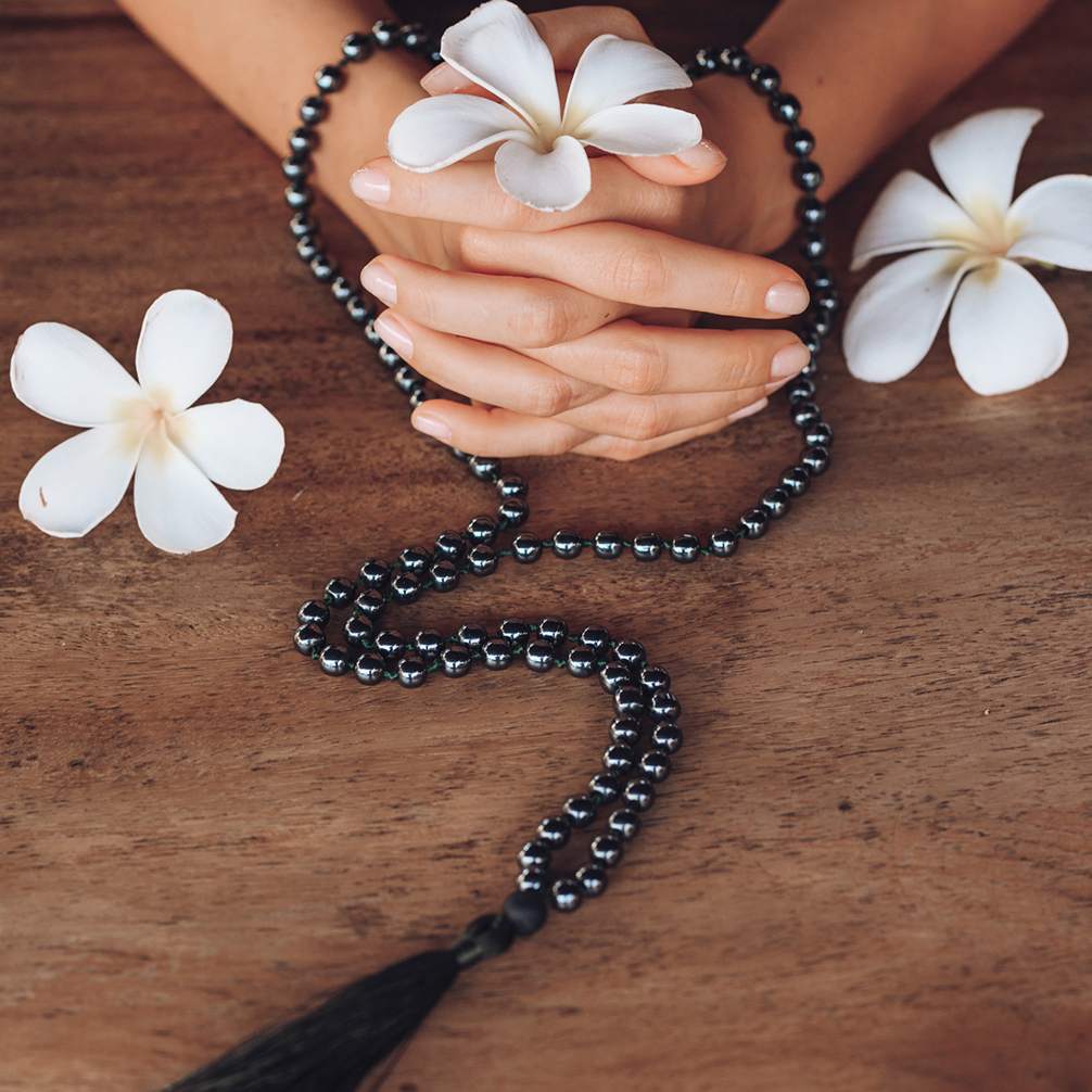 Mala beads and white flowers held in clasped hands