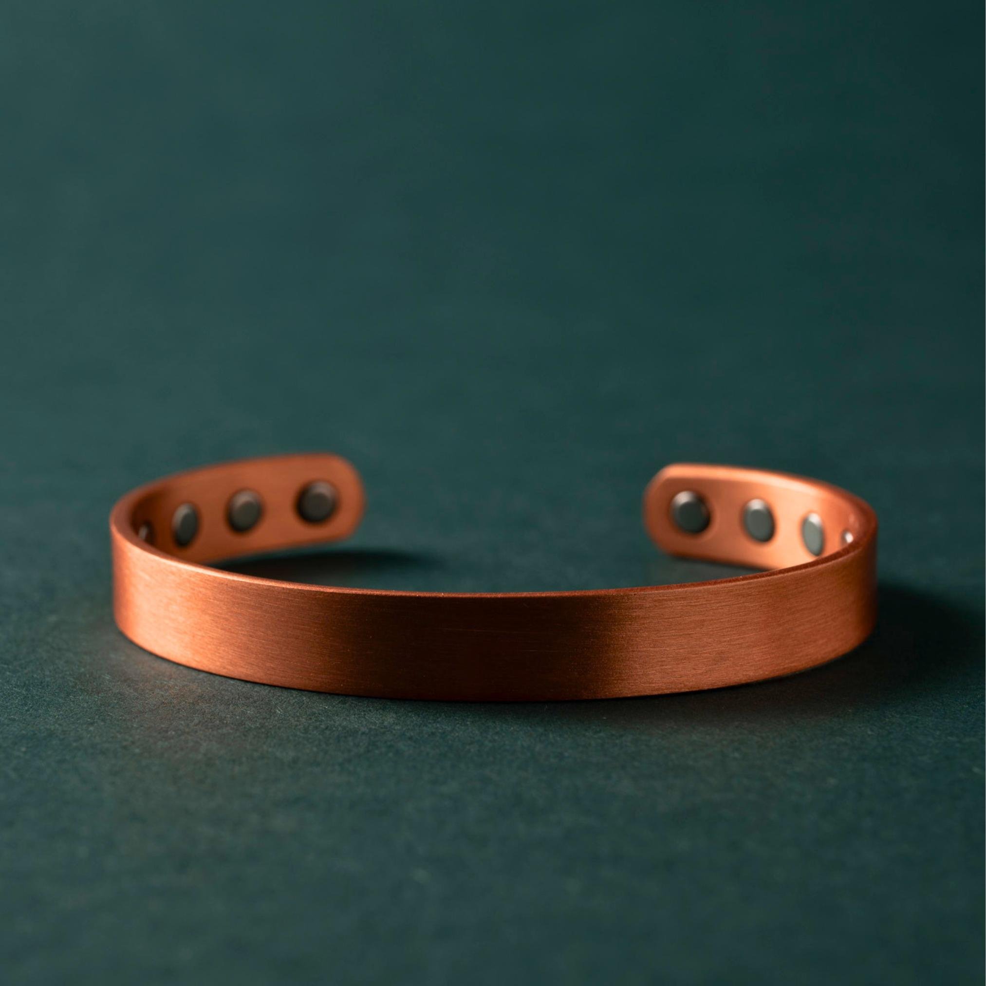 A copper magnet bracelet, full band, on a dark green surface